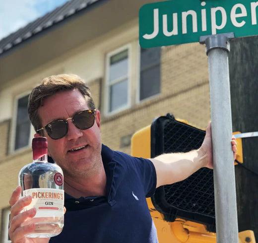 Marcus Pickering with a bottle of Pickering's Gin at a street sign called Juniper