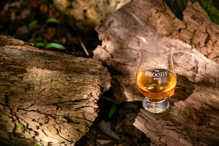 A glass of The Broody Hen outside on a tree trunk