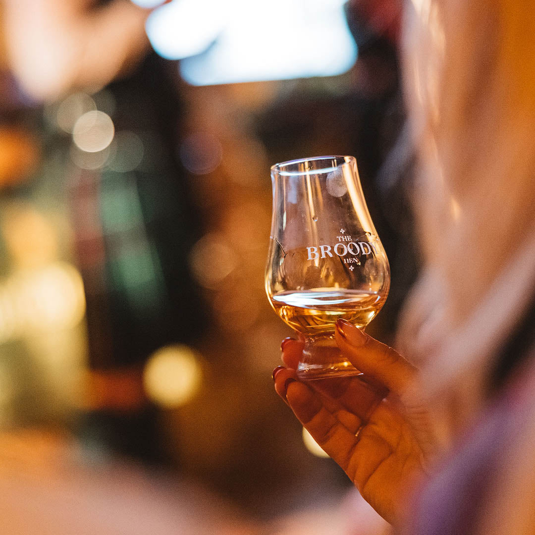 Someone holding a dram of The Broody Hen Scotch Whisky