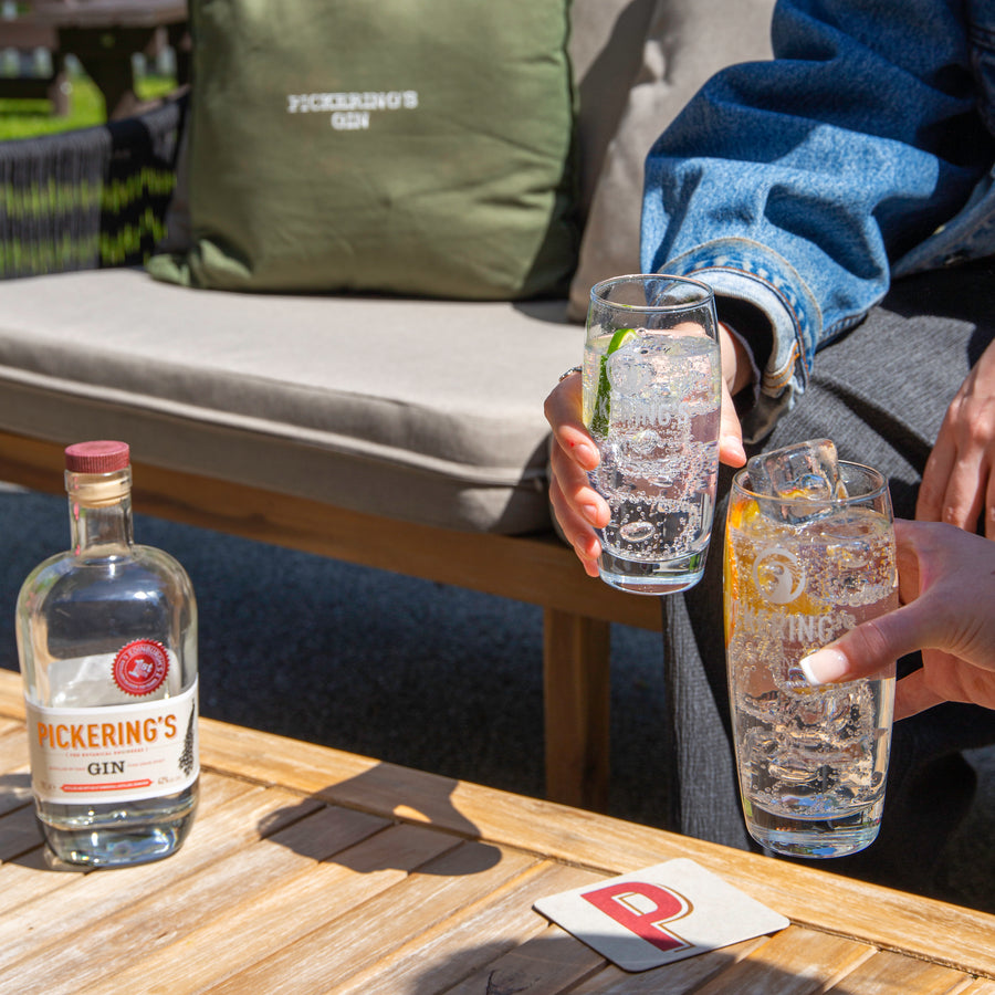 Bottle of Pickering's Gin on a table with two people cheersing next to it