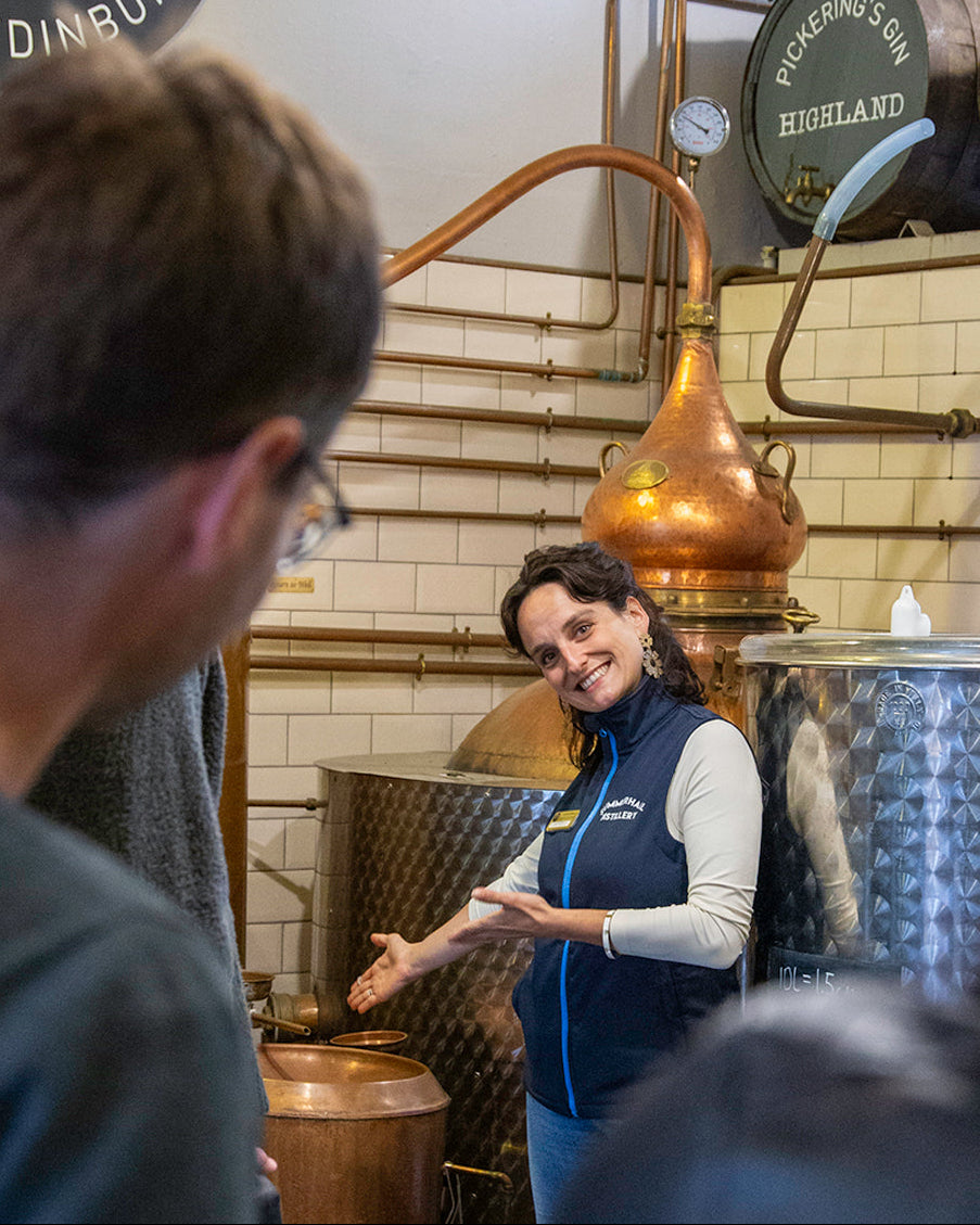 Person in a gin distillery with equipment and 'Picker's Gin' branding.