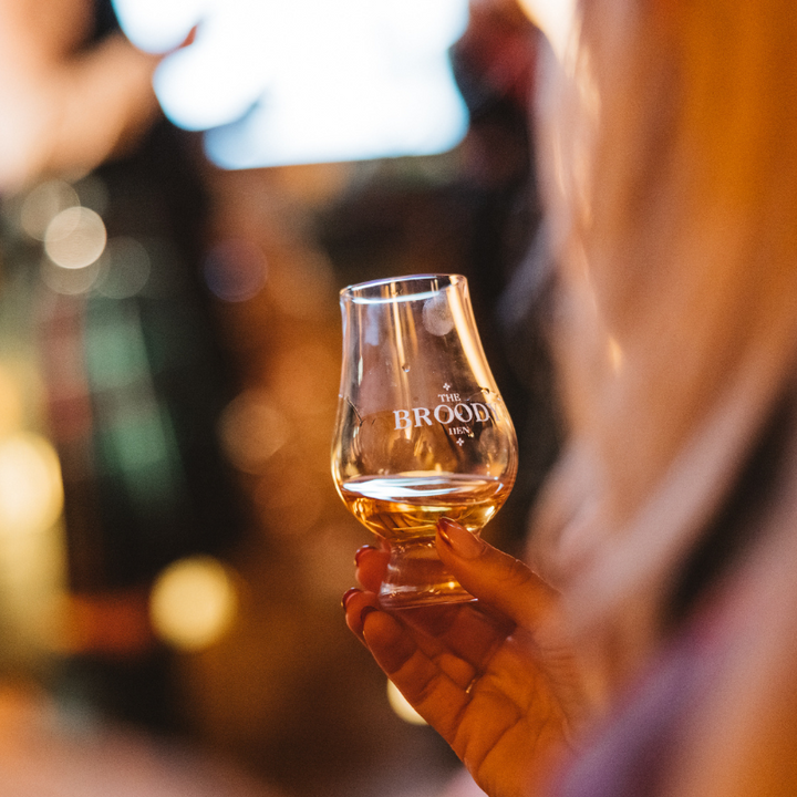 Someone holding a dram of The Broody Hen Scotch Whisky