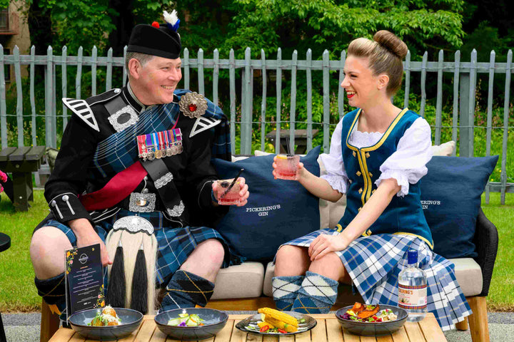 Two people in traditional Scottish attire sitting on a bench outdoors.